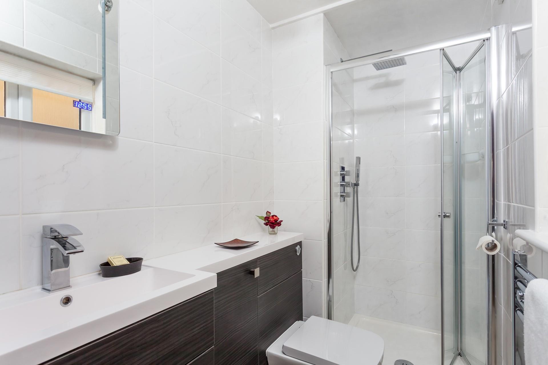 The shower room has an enclosed shower with a fixed rainfall shower head and a microphone style shower attachment.