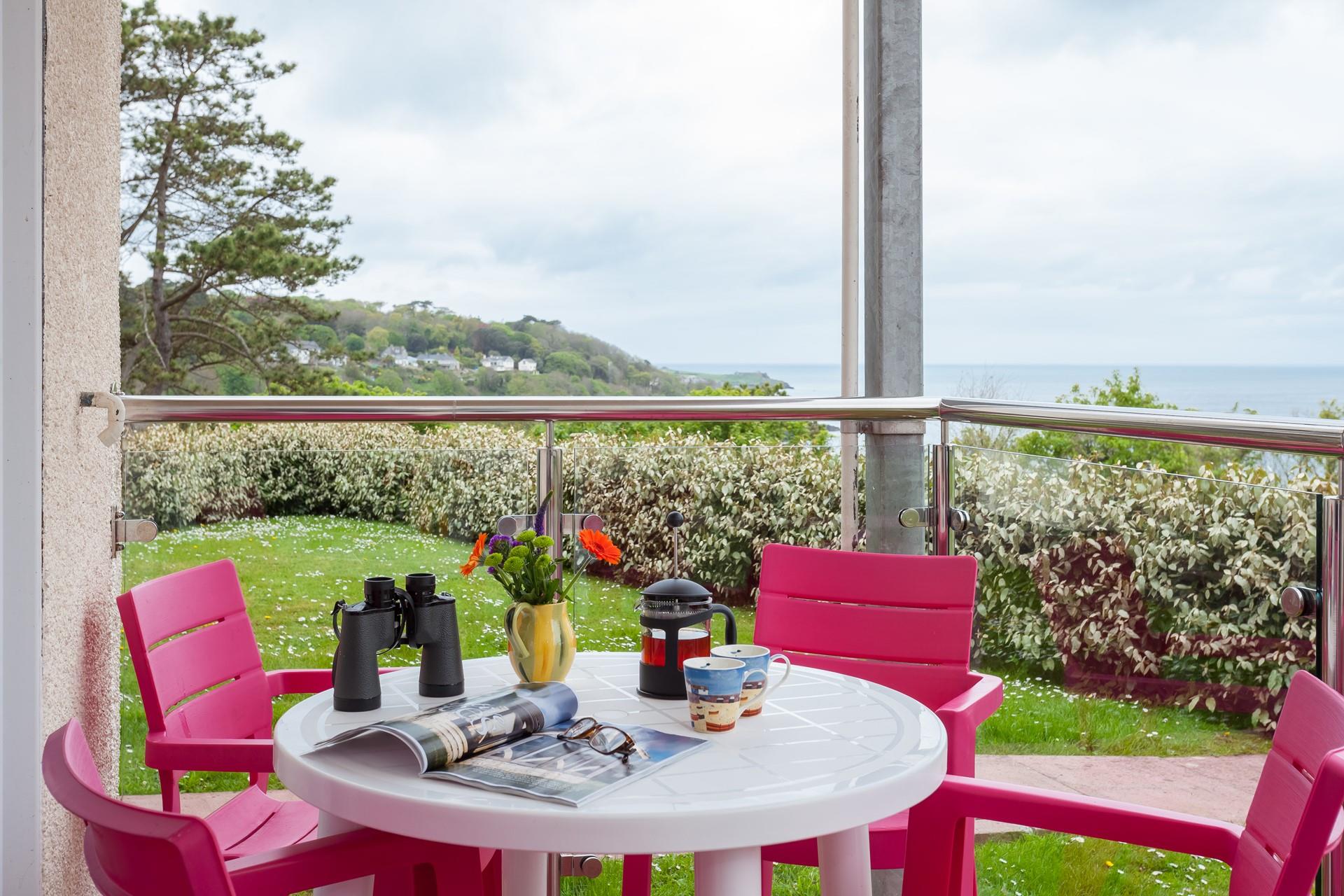 Colour pop chairs and table on the glass balustrade balcony create a cheerful setting overlooking the grass lawn and stunning sea view.