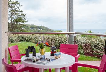 Colour pop chairs and table on the glass balustrade balcony create a cheerful setting overlooking the grass lawn and stunning sea view.