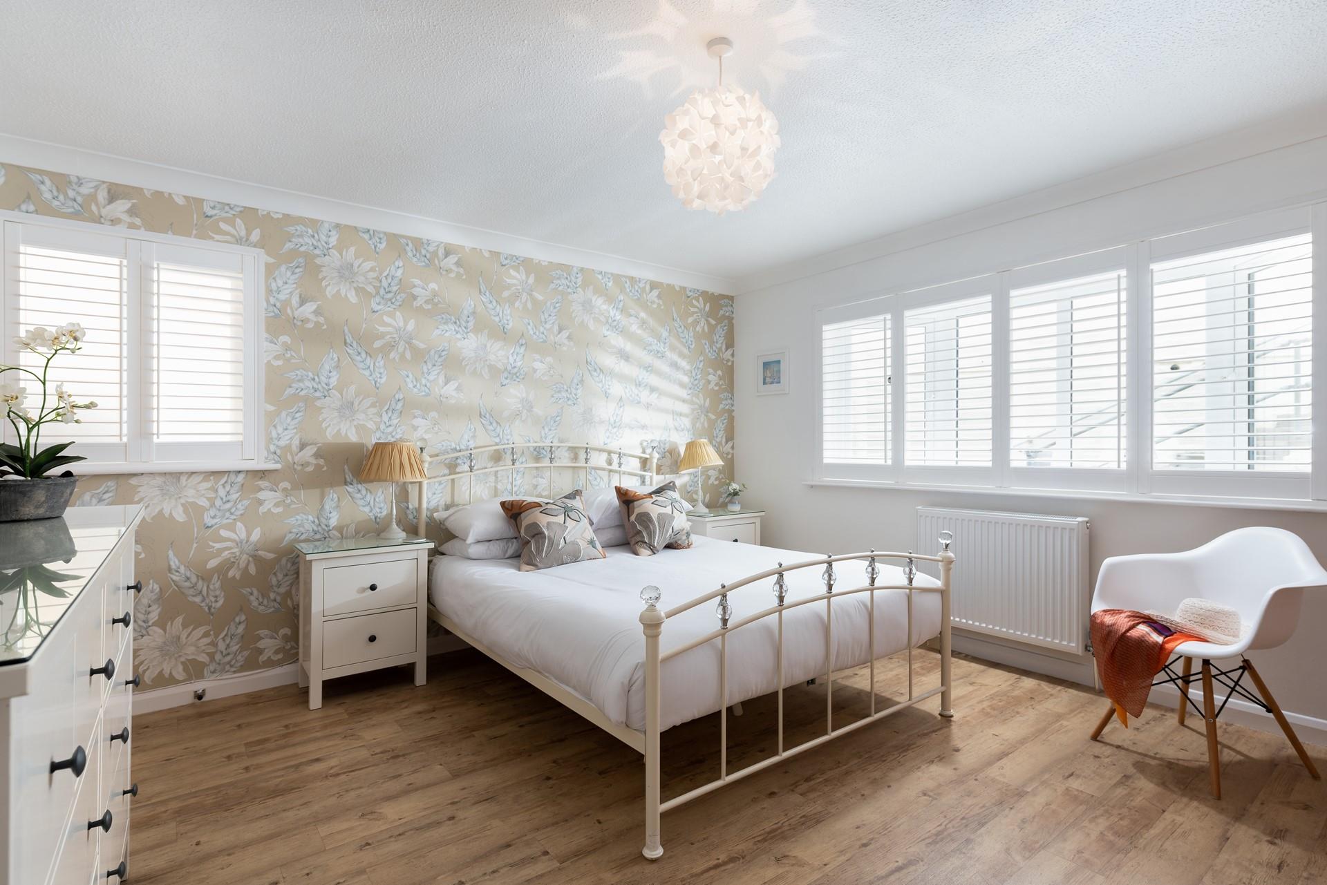 Bedroom 1 is elegantly decorated, featuring a stunning floral feature wall and simple white shutters. 