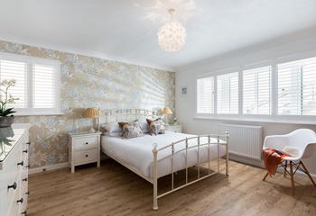 Bedroom 1 is elegantly decorated, featuring a stunning floral feature wall and simple white shutters. 