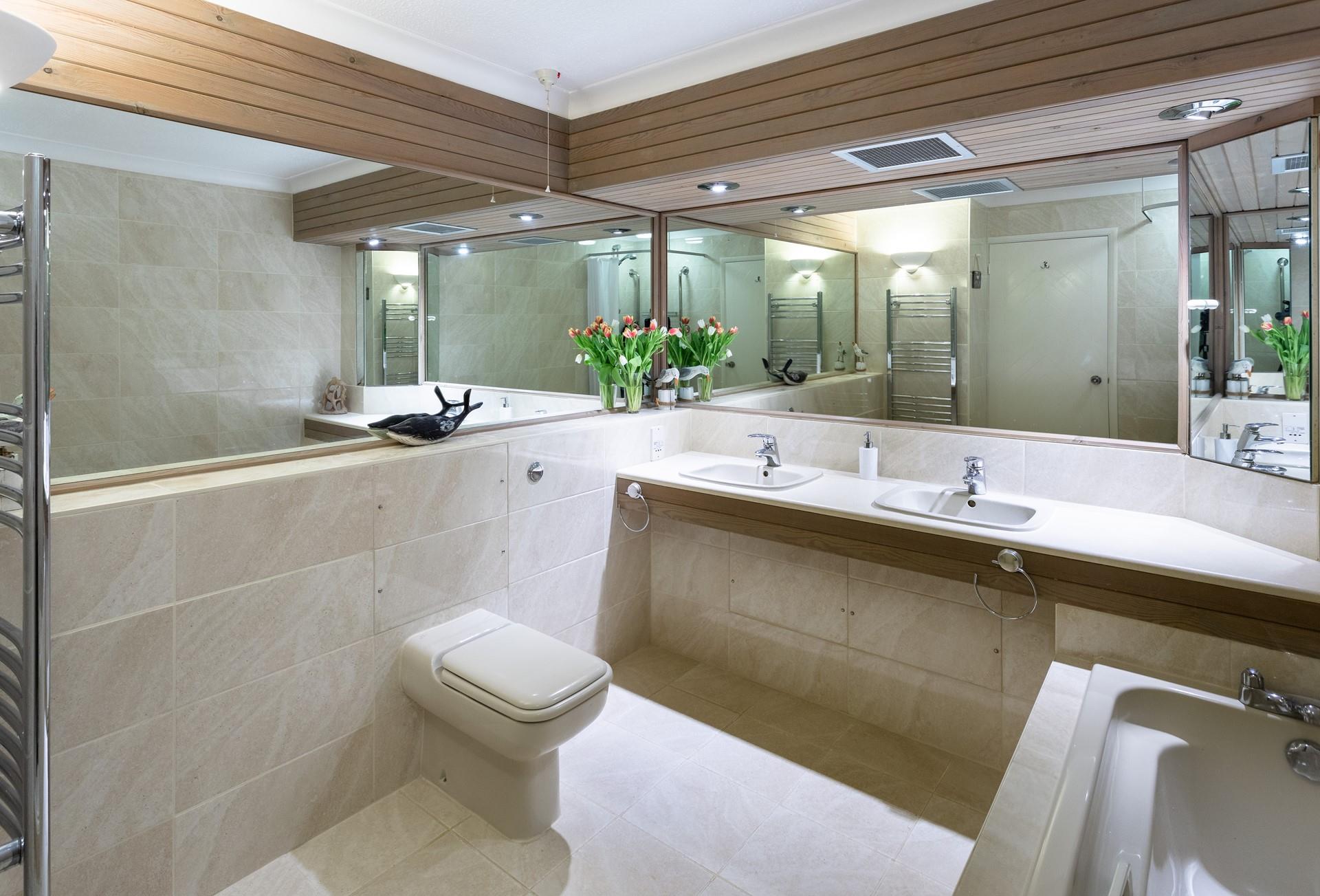 Sleek and spacious, the family bathroom features a bath, a separate enclosed shower, double washbasins, a WC and large mirrors. 