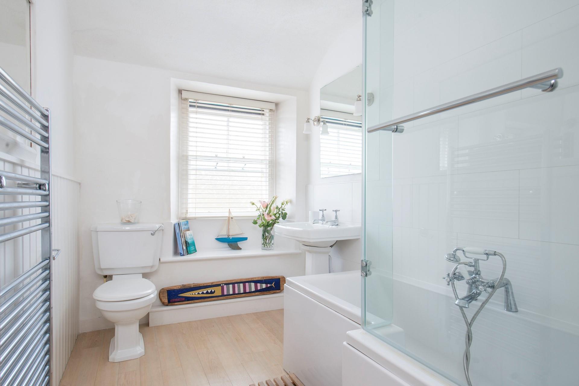 The bathroom is finished with nautical decorations, a large towel radiator and bath with shower over.