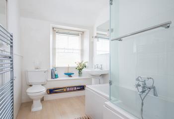 The bathroom is finished with nautical decorations, a large towel radiator and bath with shower over.