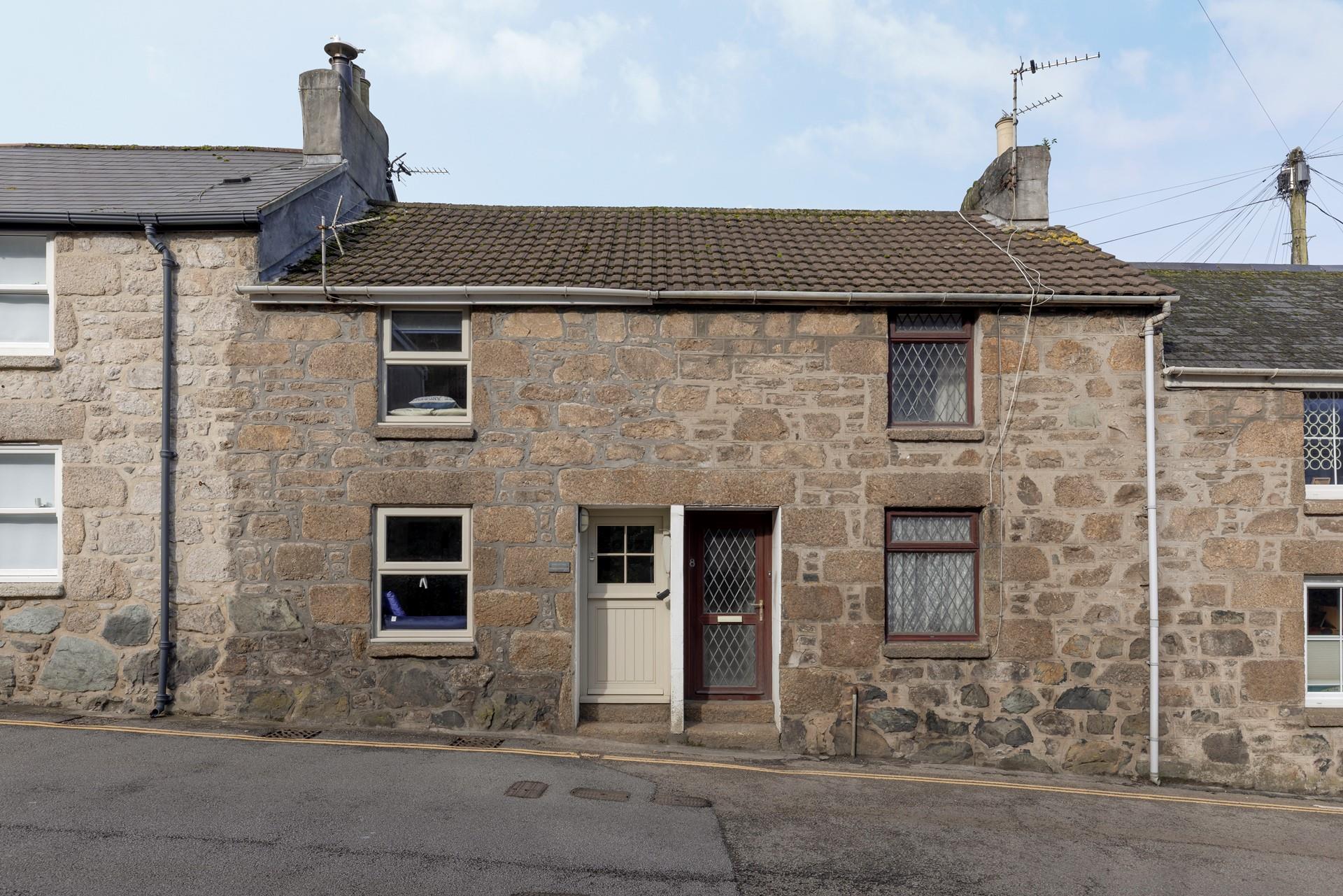 The cottage features rustic Cornish stone and a cream door and windows. 
