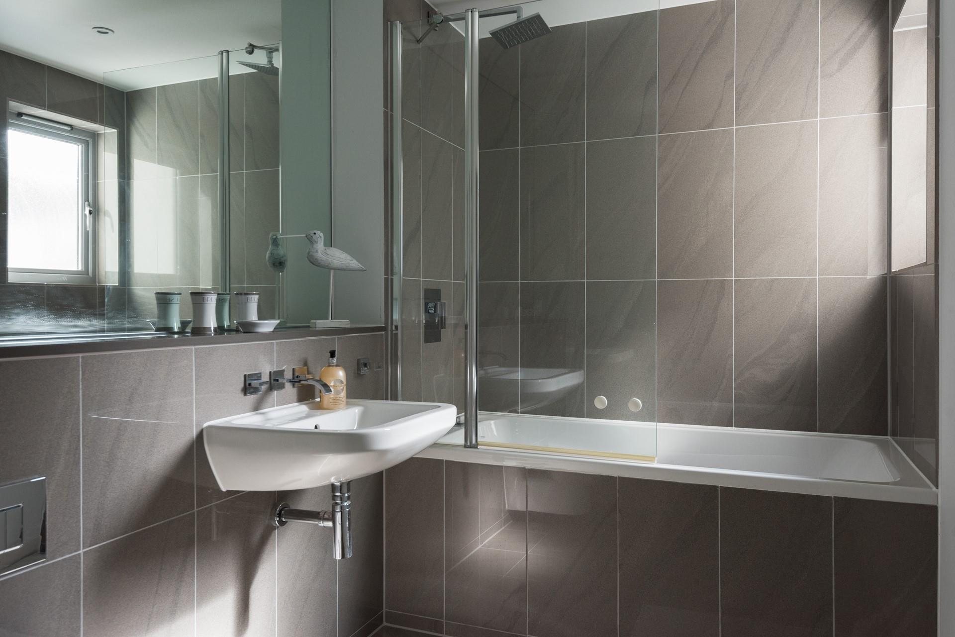 The family bathroom is sleek and modern with a bath and rainfall shower over and cosy underfloor heating.