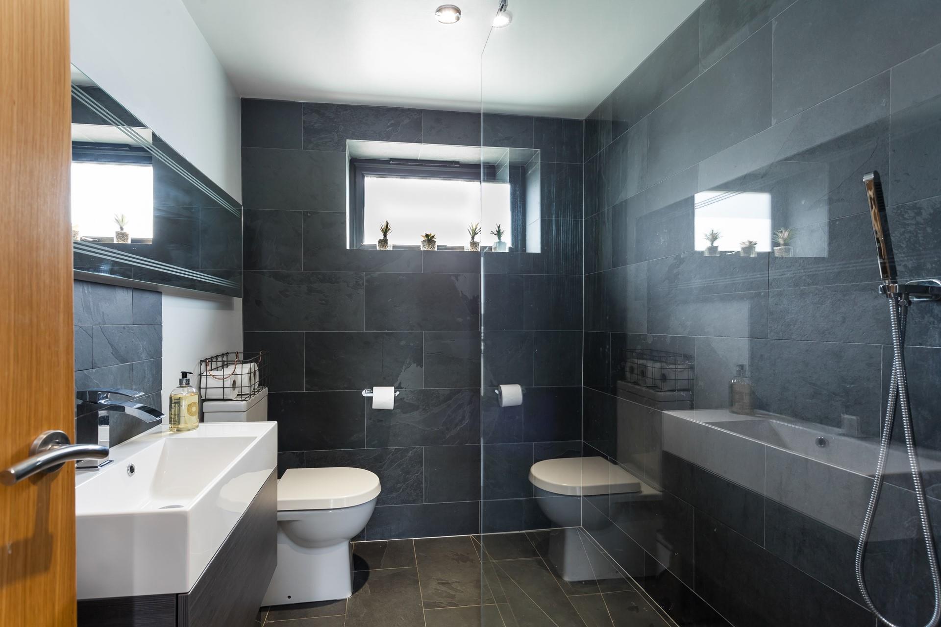 The wetroom has a simplistic walk-in shower with full slate wall and floor tiling and statement mirror above the washbasin.