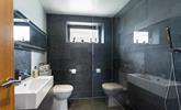 The wetroom has a simplistic walk-in shower with full slate wall and floor tiling and statement mirror above the washbasin. - Thumbnail Image