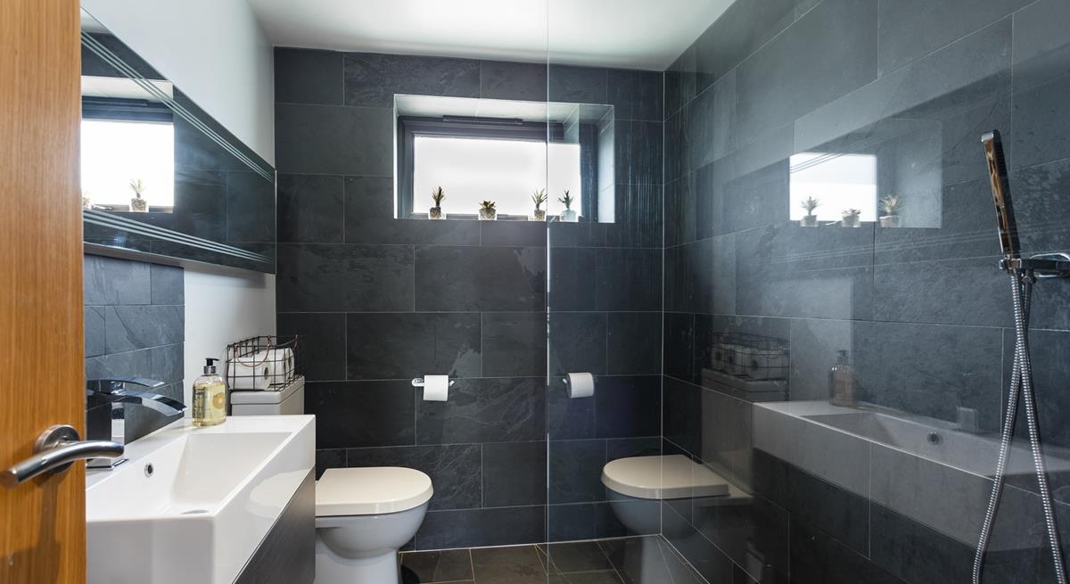 The wetroom has a simplistic walk-in shower with full slate wall and floor tiling and statement mirror above the washbasin.