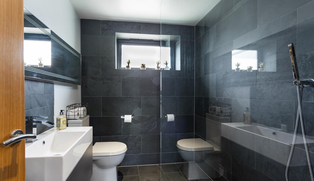 The wetroom has a simplistic walk-in shower with full slate wall and floor tiling and statement mirror above the washbasin.