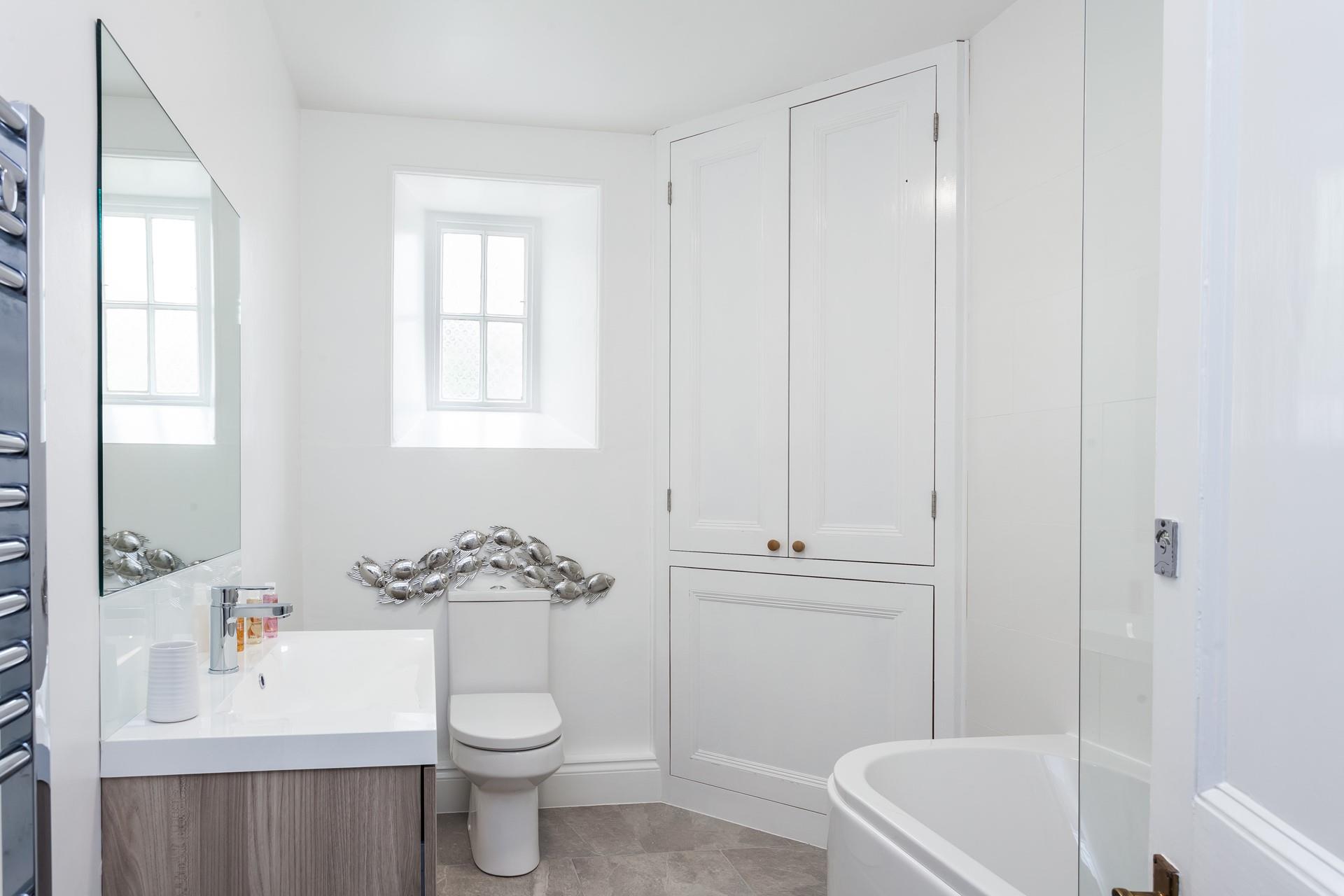 A rain shower head sits above the bath as well as there being a handheld shower attachment in this luxury bathroom. 