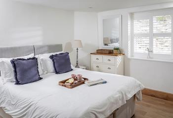 Bedroom 4 has a relaxing ambience, with soft and calming decor and a view out across the patio. 