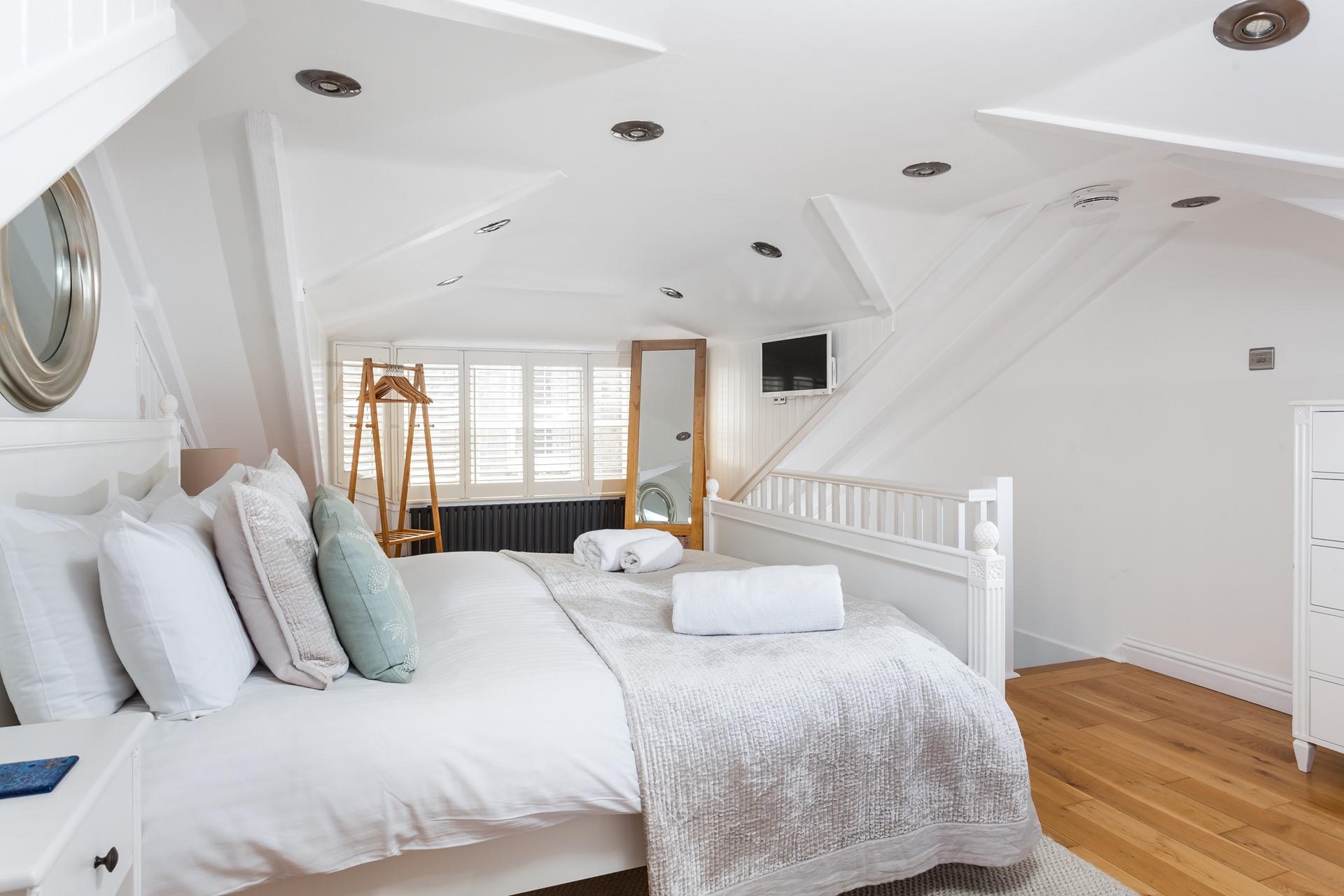 Bedroom 3 has a loft aspect with natural oak wood flooring, an easel mirror and a trestle style hanging rail.