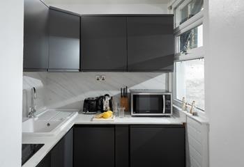 The compact kitchen is stylish and well-equipped for preparing and cooking meals.