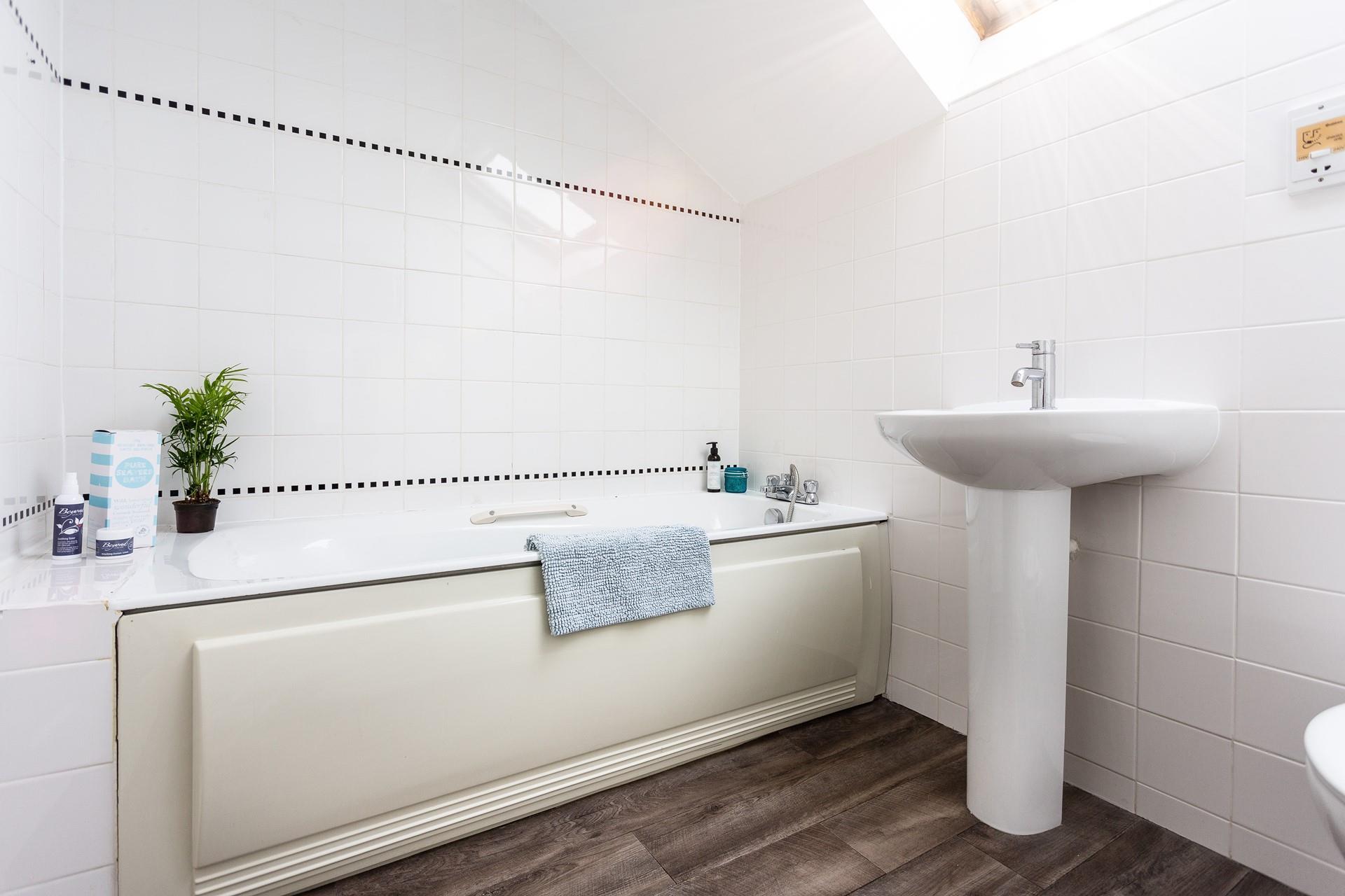 The bathroom has a modern design with a bath and handheld shower.