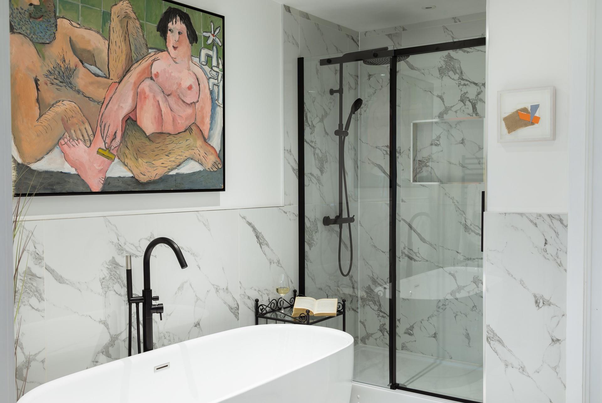 The spacious en suite bathroom has a freestanding bath, a rainfall shower, and quirky artwork.