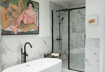 The spacious en suite bathroom has a freestanding bath, a rainfall shower, and quirky artwork.