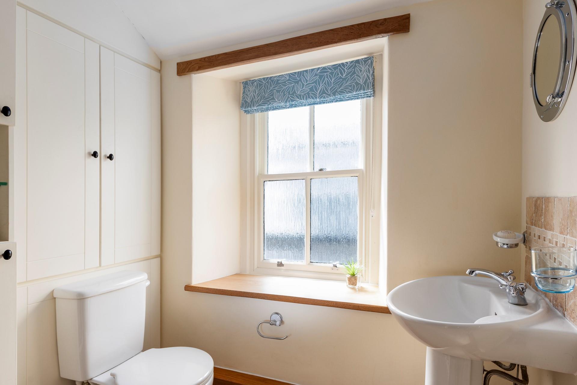 The character of the cottage continues into the family shower room, with an exposed beam and a deep window sill. 