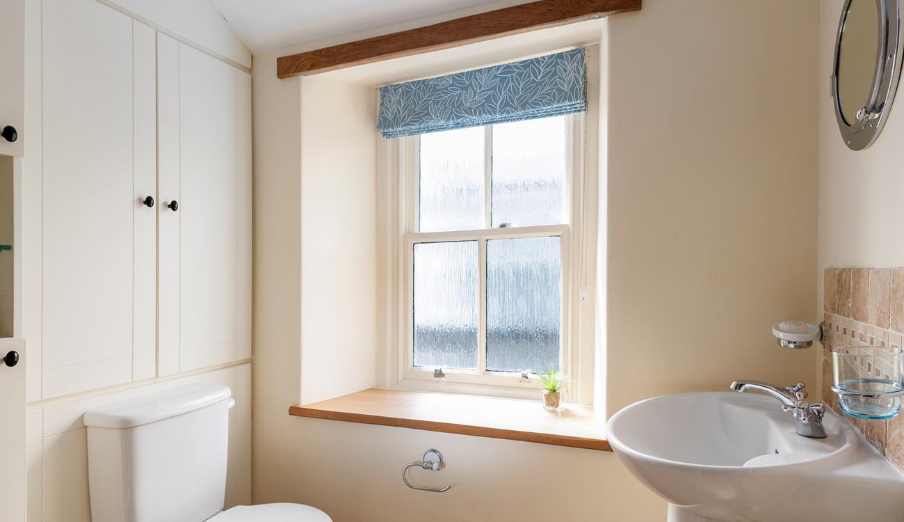 The character of the cottage continues into the family shower room, with an exposed beam and a deep window sill. 