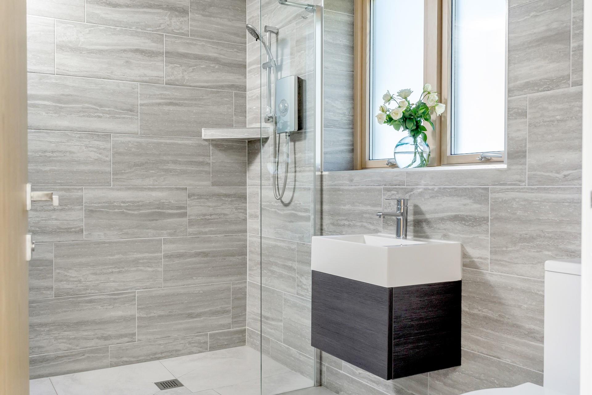 The modern en suite bathroom is decorated with stylish grey tiles and is fully accessible with a walk-in shower.
