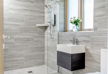 The modern en suite bathroom is decorated with stylish grey tiles and is fully accessible with a walk-in shower.