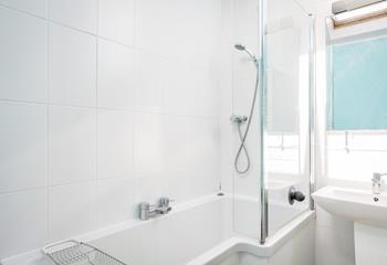 The fully tiled bathroom has a bath with a shower over.